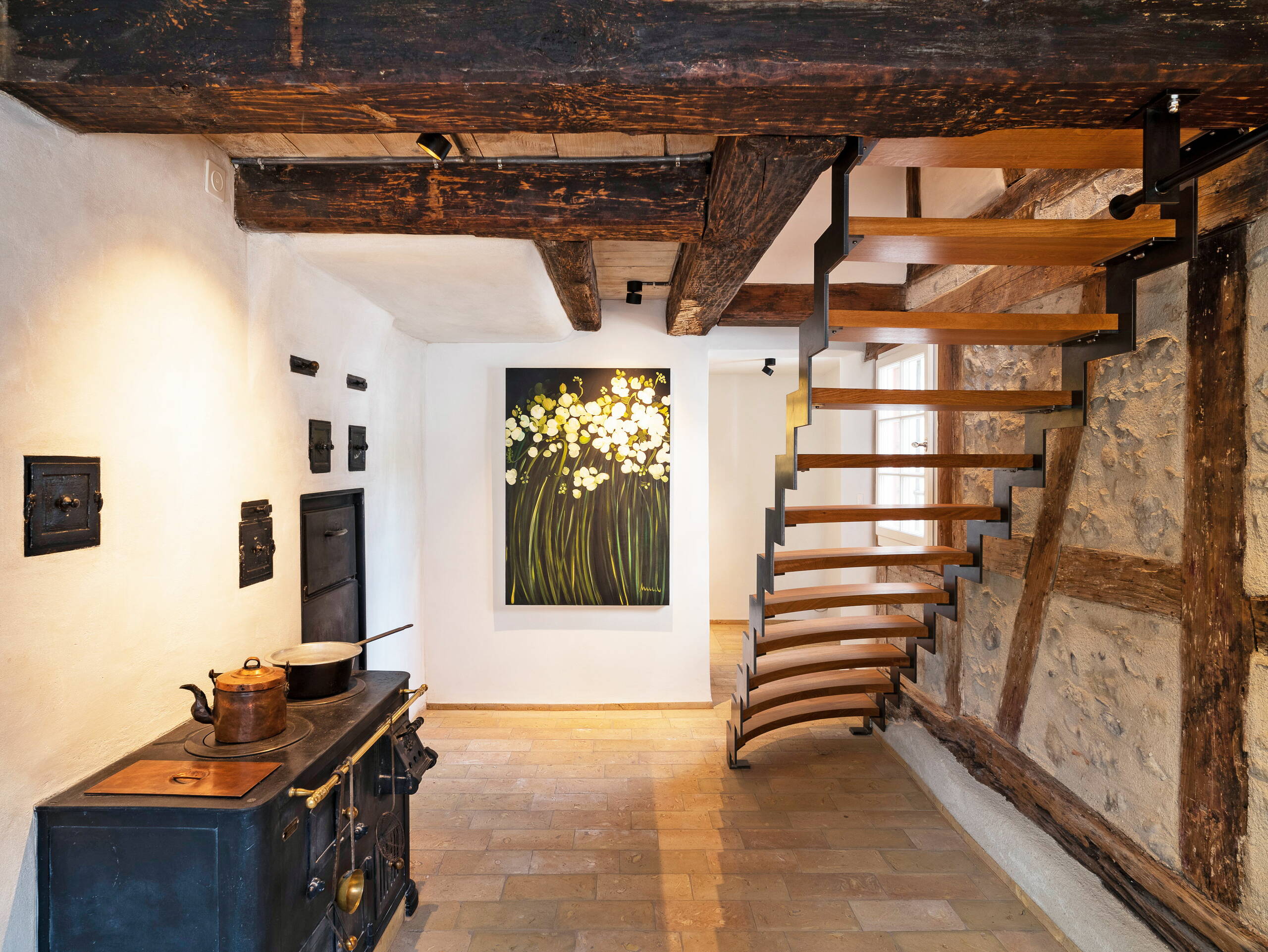 Sicht in einen Raum mit alten Holzbalken an der Decke und einer Treppe aus Holz und Metall in den zweiten Stock.
